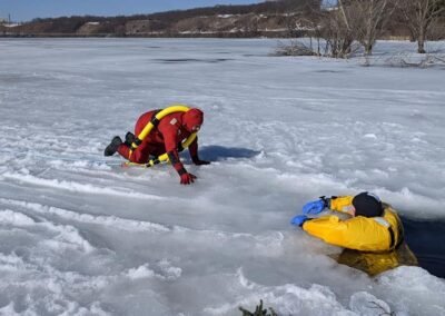 A rescuer crawls across the ice toward a person in the water