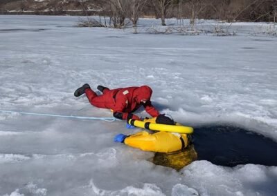 A rescuer on the ice reaches a person in the water at the edge of the hole