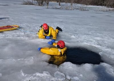 Two rescuers work at the ice hole with a rescue board nearby