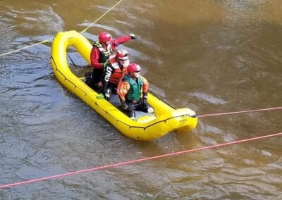 Rescuers in helmets and life jackets ride an inflatable raft along a rope line across the river