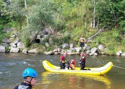 Rescuers in the raft on the river while an instructor watches from the bank